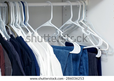 Looking inside a man\'s closet or armoire full of clothes hanging on hangers.