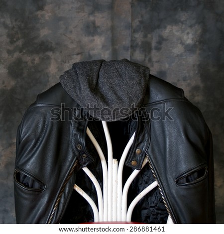 A leather biker jacket hangs on the back of a chair with a tweed cap sitting on top.