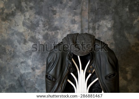 A leather motorcycle jacket hangs on the back of a chair with a tweed cap sitting on top.