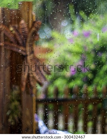 Looking through a rain soaked window out towards a colorful lush garden, focus is on rain drops on glass with garden out of focus.