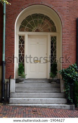 A white arched doorway in the historice section of boston called beacon hill, the arched window above the door looks like a spider web, and half circle panes adorn the sides of the door.