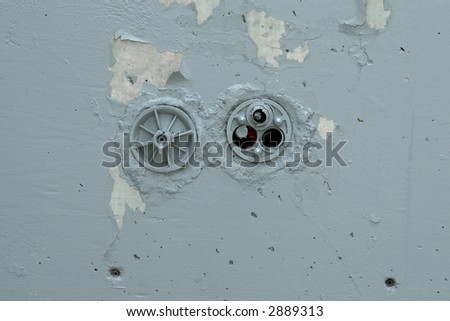 a peeling grey painted cement wall with electrical conduits in the center, one has exposed cut wires