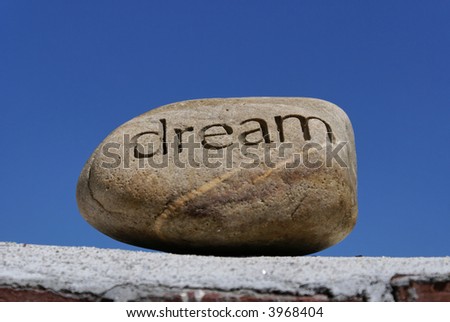 dreams put on the shelf, a rock with the word dream inscribed in it  sits on top of a brick wall against a deep blue sky