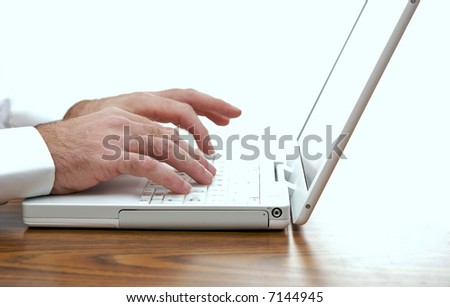 man sitting at desk typing on the keyboard of a white laptop