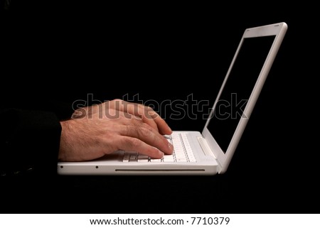 man sitting at desk typing on the keyboard of a white laptop with black background
