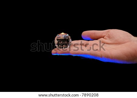 multi faceted crystal globe sitting on finger tips of a man lit from below with blue theatrical lighting against a black background