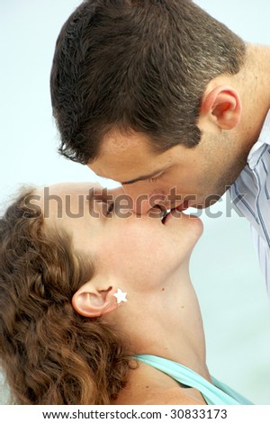 a handsome young man with short hair leans down to kiss a pretty woman with long curly hair