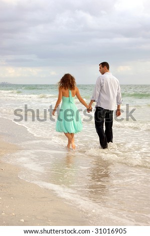 Young lovers walking away from the viewer along the water's edge at Bonita Beach, Bonita Springs Florida