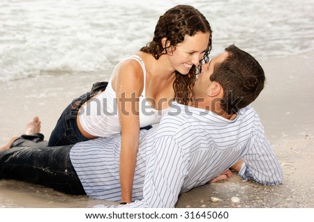 Beautiful couple laying on the beach looking into each others eyes, smiling and happy.