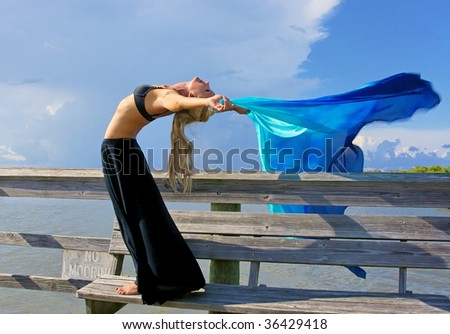 fit and attractive blonde woman is arching back making her arms horizontal as the wind blows back her veil