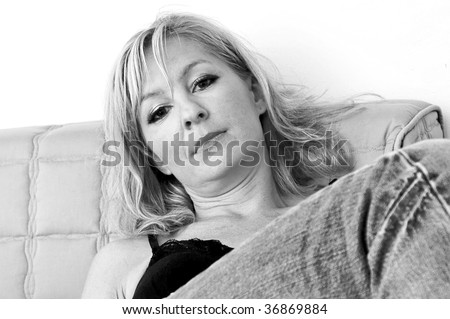 attractive woman sitting back with leg up looking directly at viewer, with head tilted, black and white image