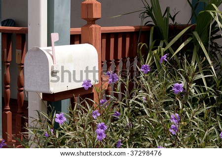 a whitish mail box with flag up among flower bed