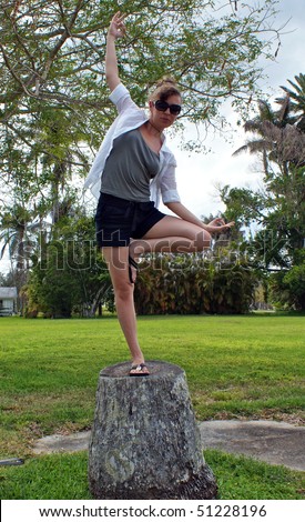Woman doing yoga tree pose on the stump of an old tree outside surrounded by trees and greenery