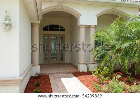 Walkway and front door to generic high end home in southwest florida with small palm tress.