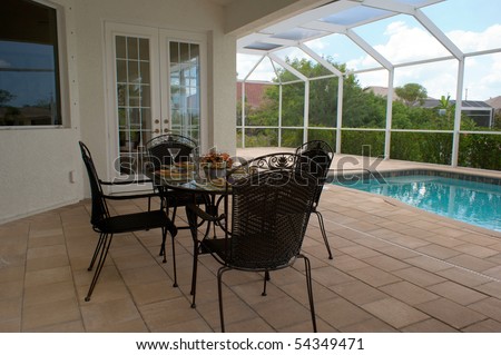 a table is set for dinner on an outside patio or lanai with swimming pool in background, the patio is screened in.