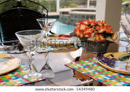 detail image of a table set for dinner on an outside patio or lanai with swimming pool in background, the patio is screened in.