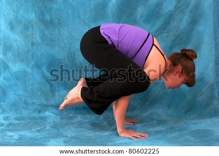 Right side view of woman in Crow yoga pose against a blue background accented with blue and red lights.