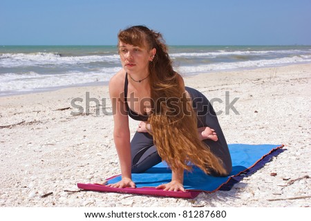an athletic brown haired woman is doing yoga exercise kneeling lotus on an empty beach at the gulf of mexico in bonita springs florida with long hair blowing in wind