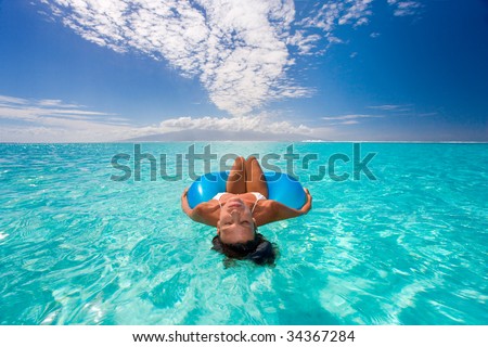 woman floats on blue inner tube in turquoise waters in tahiti with bikini on beautiful summer vacation