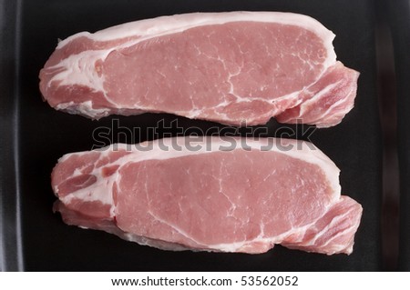 Two raw pork steaks on the black square plate macro shot