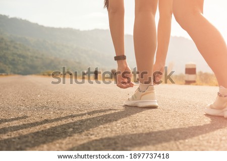 woman tying knots shoe laces,on empty road,in morning