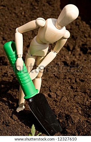 A wooden mannequin digging in the garden