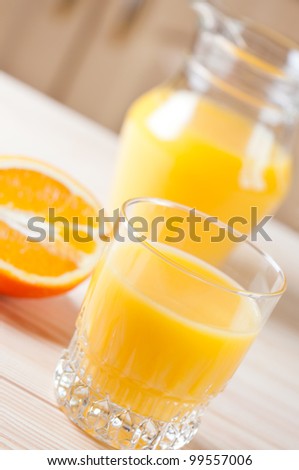 Glass of juice on table in background pitcher and orange.