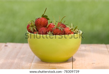 Strawberries with bowl on wooden table outdoor