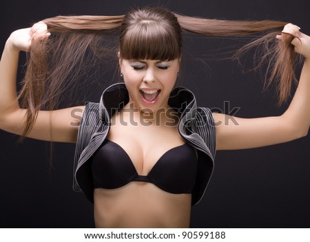 Beautiful young woman pulling in different directions her hair and shouts . Black background