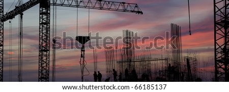 silhouettes of construction workers, construction equipment and elements of a building under construction at Sunset