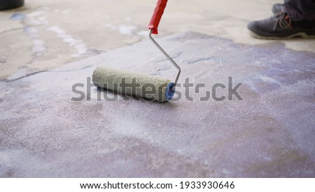 Priming the concrete floor with a roller. Professional floor primer. Leveling concrete floors. Floor repair using a primer.