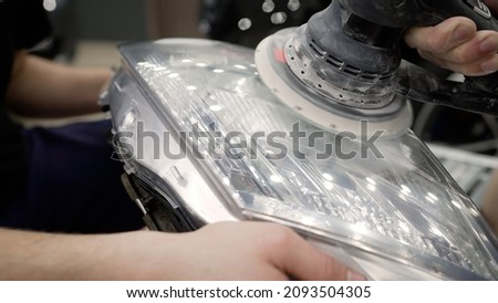 The master polishes the headlight. The master mechanic polishes the car with a polisher, detailing the series. Master repairman polishing headlight of car using special machine closeup. 