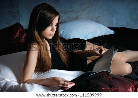 Young woman on the bed reading a magazine