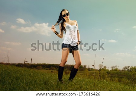 Woman in wet t-shirt, jeans and high boots standing on the field