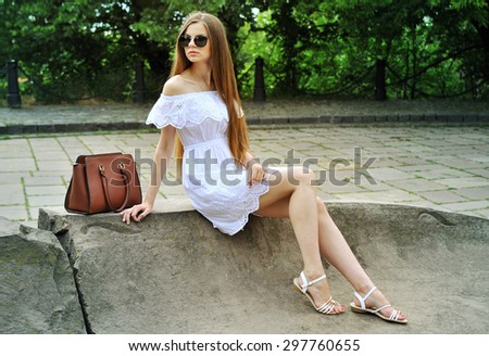 Young woman in white dress and sunglasses with bag on the street