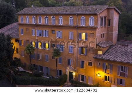 Orange glow of lights bring out the vivid colors of the apartment building in Rome, Italy. Palm trees in the foreground.
