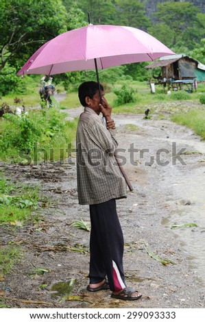 KOH SAMUI, THAILAND - OCTOBER 23, 2013: Lonely old asian man, mahout, with stick pursuer in hand, stands under umbrella  on  elephant trekking road.