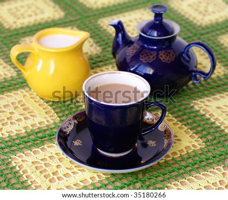 cup of beverage, jug with milk and teapot on back plane