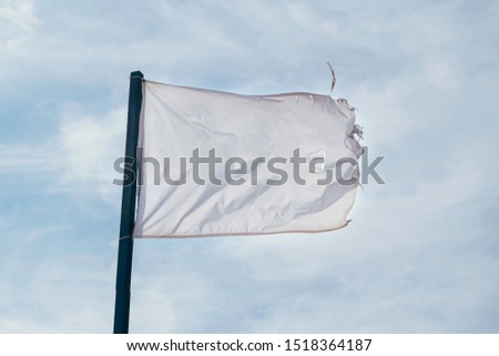 Old old, shabby, full of holes, dirty white flag waving with the wind against sky clouds. Stock fotó © 