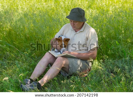 Mature man and young dog reading interesting book under tree shadow