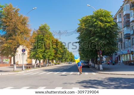 Kremenchuk, Ukraine - AUGUST 23, 2015: Young bicycle rider cycling with Ukrainian flag on central city street on the eve of Independence Day