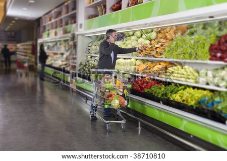 Man calling by cellular phone while picking vegetables in a supermarket. All recognizable logos and brands have been retouched or blurred out.