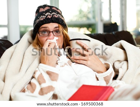 Sneezing and blowing her nose, a young woman struggles with a head cold