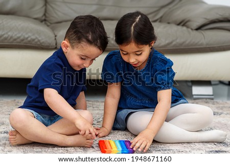 Two cute children playing with the Pop It fidget. Push pop bubble flexible fidget sensory toy provide discharge and are good for the development of kid. Soft focus.