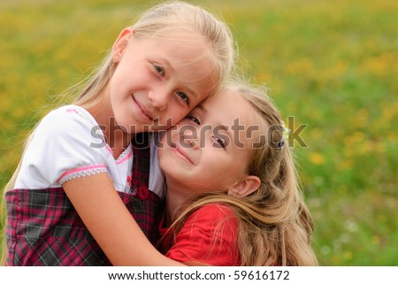 Two sisters hug one another outdoors, happy family