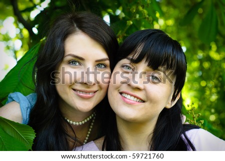 Two sisters hug one another outdoors, close up faces