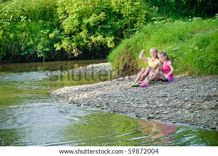 Two sisters throw stones into the river, have fun.