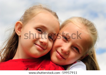 Two sisters hug one another outdoors, happy family. Close up faces.