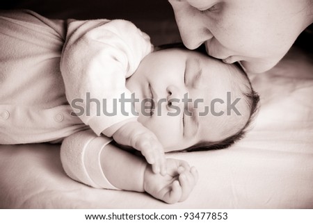 Sleeping newborn baby closeup face with mother kissing