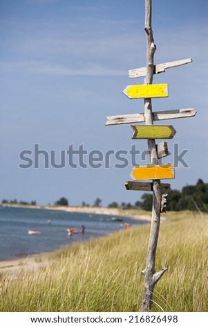 A wooden sign post pointing in all directions on a lake beach in the summer.